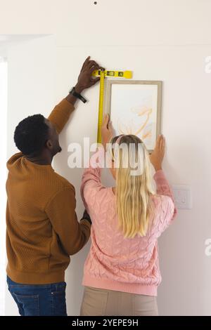 multiracial couple measuring wall for picture frame at home, working together. Home improvement, teamwork, renovation, collaboration, lifestyle Stock Photo
