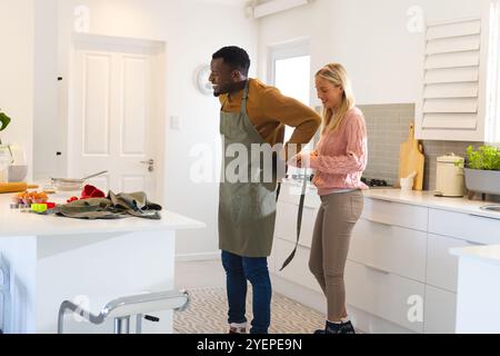 In kitchen, multiracial couple preparing for cooking, tying apron with smiles, at home. domestic life, bonding, lifestyle, culinary, happiness, teamwo Stock Photo