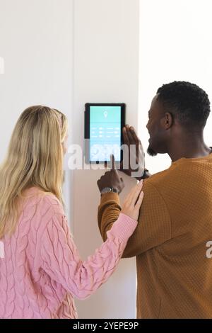 multiracial couple using smart home device, adjusting settings with touchscreen at home. Technology, automation, domestic, lifestyle, innovation Stock Photo