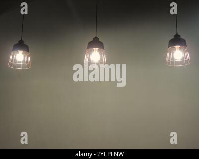 three glowing lamps on long cords against the wall as an element of room decor, electric light equipment in the structure of interior design Stock Photo