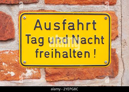 Yellow sign Exit keep clear day and night on a reddish brick wall, Germany Stock Photo