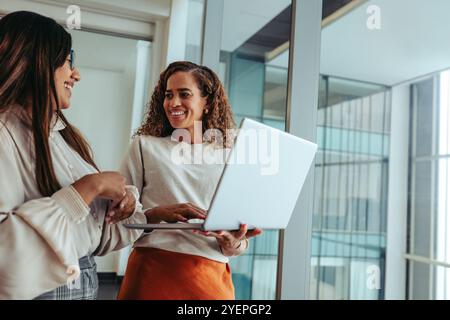Two female professionals engage in a collaborative discussion in a bright, modern office setting. The women, both smiling and engaged, are exploring i Stock Photo