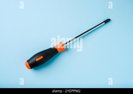 Orange and black rubber-handled Phillips screwdriver on blue background Stock Photo