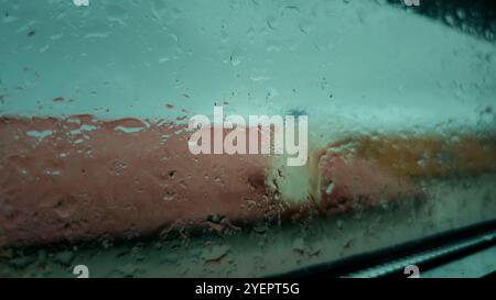 Blurry rain drops falling down on window at home. Sky drops. Close up of slow rainning. Moody weather day. Stock Photo