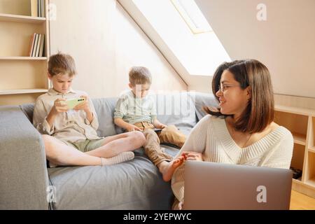 The woman works from home, and the children are playing on the phone Stock Photo