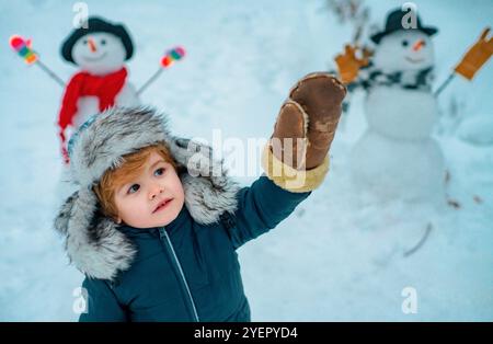 Child boy Having Fun in Winter Park. Winter clothes for kids. Happy winter time. Beauty child with snowman in frosty winter Park. Stock Photo