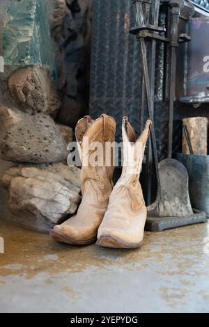 Pair of worn cowboy boots beside a rustic stone and metal backdrop Stock Photo