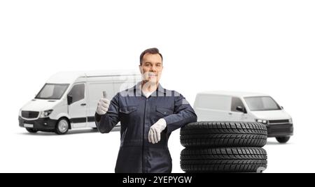 Auto mechanic worker with vans leaning on a pile of tires and showing a thumb up gesture isolated on white background Stock Photo