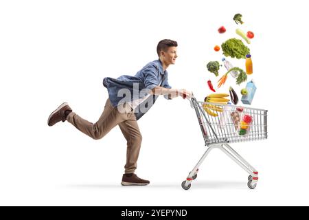 Full length profile shot of a guy running fast with a shopping cart with groceries falling inside isolated on white background Stock Photo