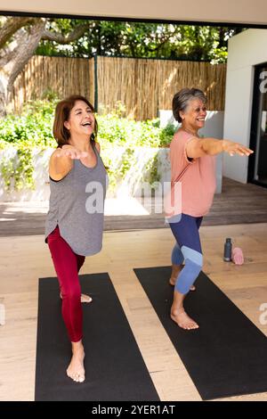 Senior female friends practicing yoga together outdoors, smiling and enjoying moment. meditation, wellness, mindfulness, exercise, friendship, nature Stock Photo