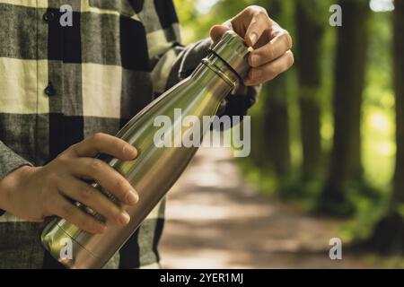 Close-up of Unrecognizable female hand holding Water bottle. Reusable steel thermo water bottle in park. Sustainable lifestyle. Plastic free zero wast Stock Photo