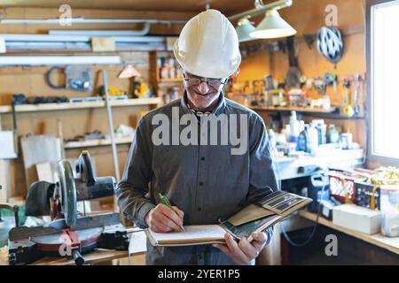 Selective focus on Inspector in the garage interior during an inspection. middle aged caucasian man wearing helmet writes notes on a notebook Stock Photo