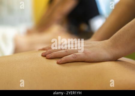 A close up shot on the hands of a Swedish massage student rubbing the back of a caucasian person, with blurry background and copy space to top Stock Photo