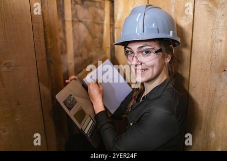 Indoor air quality inspector woman looking for molds or fungi problems on wooden walls and taking notes using her clipboard. she happy and smiling Stock Photo