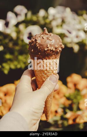 Female hand holding delicious american vanilla chocolate ice cream. Tasty homemade icecream Gelato in the waffle cone. Gluten free vegan dairy free ic Stock Photo