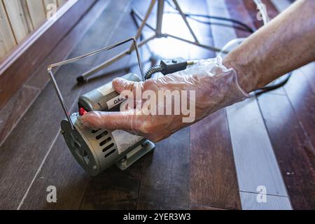 A close up on the hands of a man wearing protective gloves, operating a small portable gas pump during an indoor home quality assessment Stock Photo