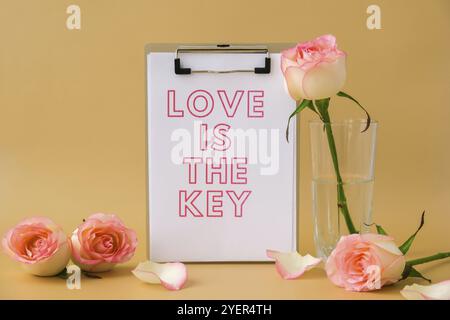 LOVE IS THE KEY text on greeting card paper note. Delicate pink roses on beige background. Minimal trendy composition. Romantic pastel pink rose flowe Stock Photo