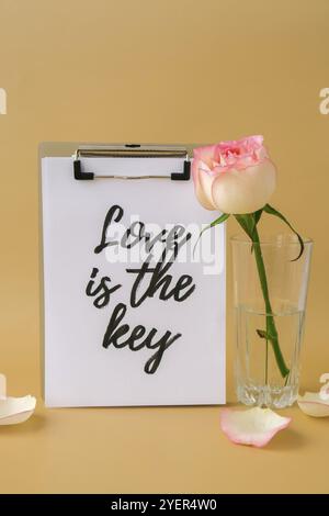 LOVE IS THE KEY text on greeting card paper note. Delicate pink roses on beige background. Minimal trendy composition. Romantic pastel pink rose flowe Stock Photo