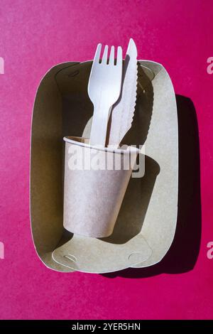 Wooden forks and paper cups with plates on color background. Eco friendly disposable tableware. Used in fast food, restaurants, takeaways, picnics. No Stock Photo