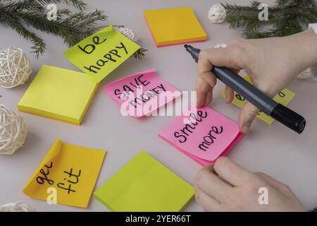 Unrecognizable woman writing new year's resolutions on colorful sticky notes. Making promises for new year, setting goals. Creating vision board motiv Stock Photo