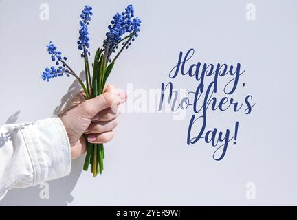 HAPPY MOTHERS DAY Female hands holding blue muscari flowers. Gift from child for mothers day. Small bouquet blue muscari. Florist in flowers shop. Spr Stock Photo