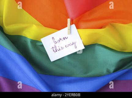 Rainbow flag with text BORN THIS WAY message on paper note. Rainbow lgbtq flag made from silk material. Symbol of LGBTQ pride month. Equal rights. Pea Stock Photo