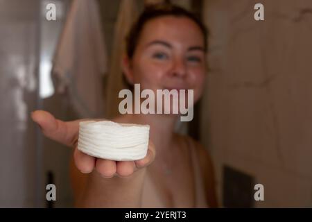 Young woman holding a round piece of cotton in a bathroom setting during daytime Stock Photo