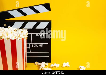 Horizontal image of popcorn with wooden clapperboard on a yellow background with popcorn scattered around, cinema and entertainment concept Stock Photo