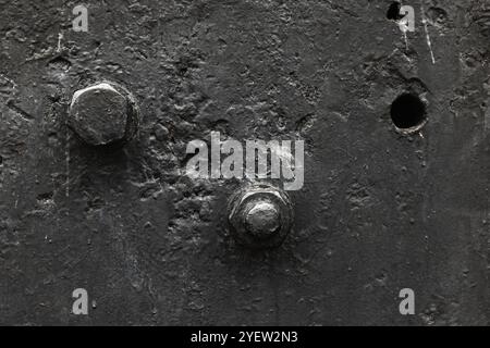 Fragment of vintage black industrial machine, close up black and white photo of bolts in frontal plate, abstract heavy industry background texture Stock Photo