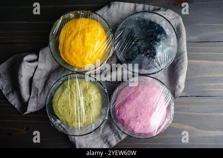 Colorful Balls of Risen Bread Dough Covered with Plastic Wrap: Yellow, black, green, and purple bread dough made with natural food colorings Stock Photo