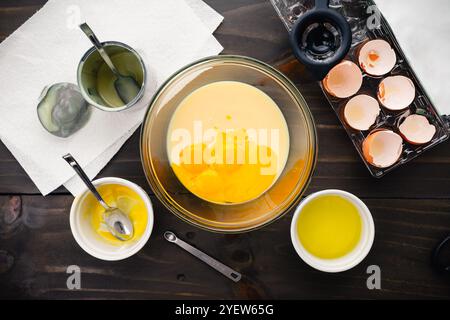 Egg Yolks and Sweetened Condensed Milk in a Glass Mixing Bowl: Custard being made surrounded with egg shells in an egg carton and kitchen equipment Stock Photo