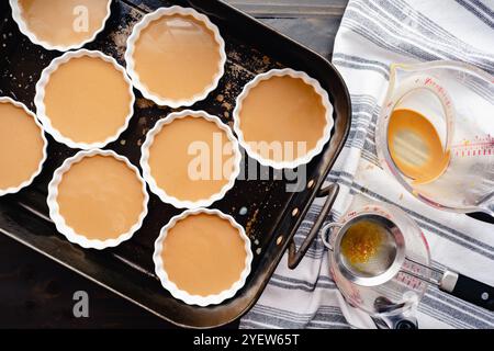 Unbaked Coffee Creme Brulees in Shallow Ramekins: Eight white ceramic ramekins filled with strained coffee creme brulee in a large roasting pan Stock Photo