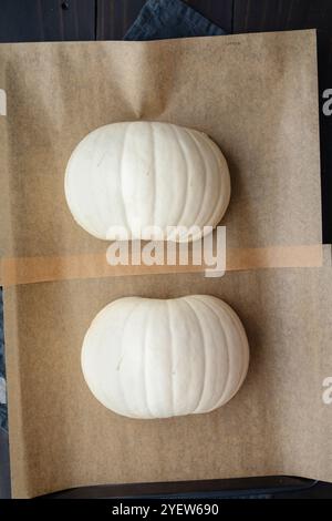 Seeded and Halved White Pumpkin on a Sheet Pan: Halves of a snowball pumpkin rubbed with coconut oil and sprinkled with pink salt on parchment paper Stock Photo