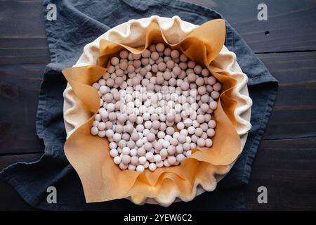 Preparing to Blind Bake a Fluted Pie Crust: Pie crust lined with parchment paper and filled with ceramic pie weights for blind baking Stock Photo