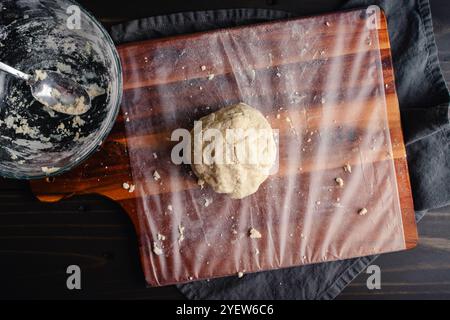 Ball of Homemade Pie Crust Dough on a Cutting Board: Freshly made pie crust dough on a messy plastic-wrapped wooden chopping board Stock Photo