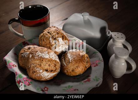 Classic farm country bread buns in a cute basket next to a mug, butter, salt, pepper. These homemade rustic rolls balls are made of organic wholemeal Stock Photo