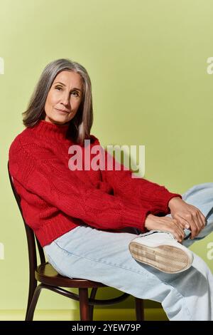 A beautiful mature woman with grey hair effortlessly embodies winter style in a cozy red sweater. Stock Photo