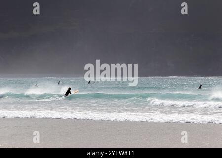 man riding a surfboard into waves on keel beach Achill island, county mayo, republic of ireland Stock Photo