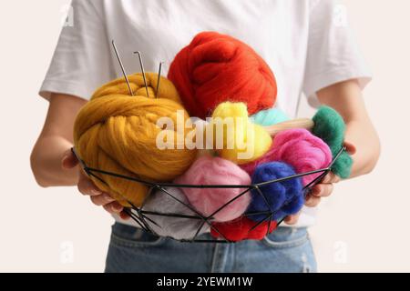 Woman holding basket with different wool for felting and needles on light background, closeup Stock Photo