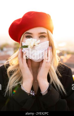 Beautiful woman in red beret holding white flower wearing surgical mask Stock Photo