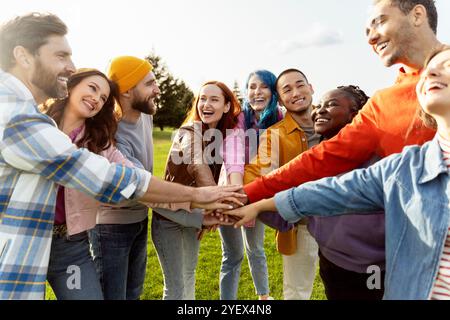 Group of diverse young people are standing in a circle on a green lawn, joining their hands together and laughing Stock Photo
