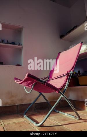 A weathered red folding chair illuminated by the light of sunset, in the room of a farm house in the eastern Andean mountains of central Colombia. Stock Photo