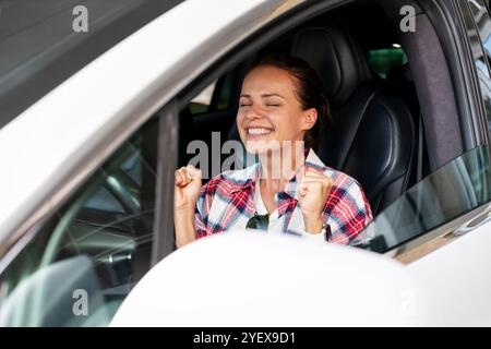 Joyful woman sitting inside her new car, celebrating her purchase. Stock Photo