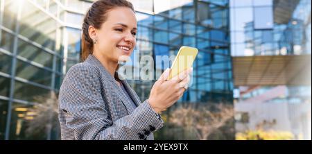 Corporate networking. Businesswoman communicate with colleges using her smartphone. Female business person using smartphone outdoors of the office bui Stock Photo