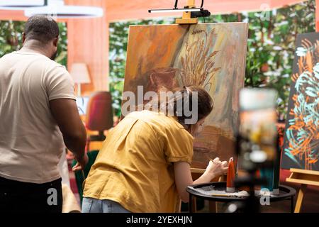 Skilled painters working together on an artwork in artistic workshop, recording an online tutorial and teach how to use creativity to paint. Documenting the creative process for virtual classroom. Stock Photo