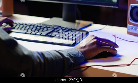 Keyboard and mouse used by gamer competing in online multiplayer videogame at home, close up. Focus on computer peripheral utilized by man playing on gaming PC in neon illuminated apartment, camera A Stock Photo