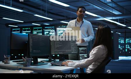 Team of researchers in data center monitoring security threats using PC, implementing cybersecurity measures. Teamworking colleagues ensuring compliance with regulations, camera B Stock Photo