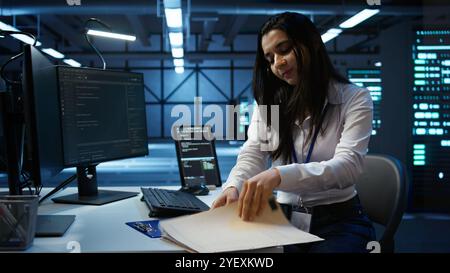 Programmer in data center arriving in office, being tasked with ensuring system can handle networking tasks. IT specialist in server farm starting job shift, tracking network traffic with PC, camera B Stock Photo