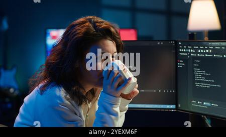 Portrait of happy computer engineer enjoying hot tea while implementing security measures to protect company systems and data. Joyful IT worker holding coffee mug and debugging code, camera A Stock Photo
