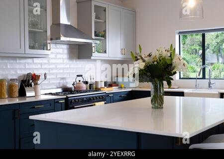 Modern kitchen with elegant white countertops and fresh flowers in vase, at home Stock Photo